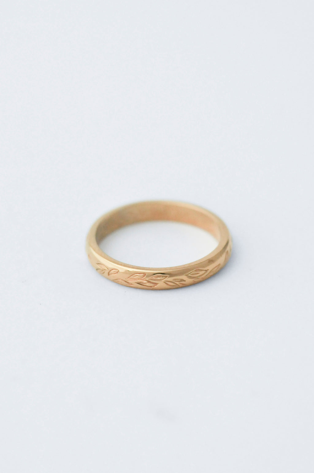 Gold wedding band ring with willow leaf hand engraved detailing on a light grey background