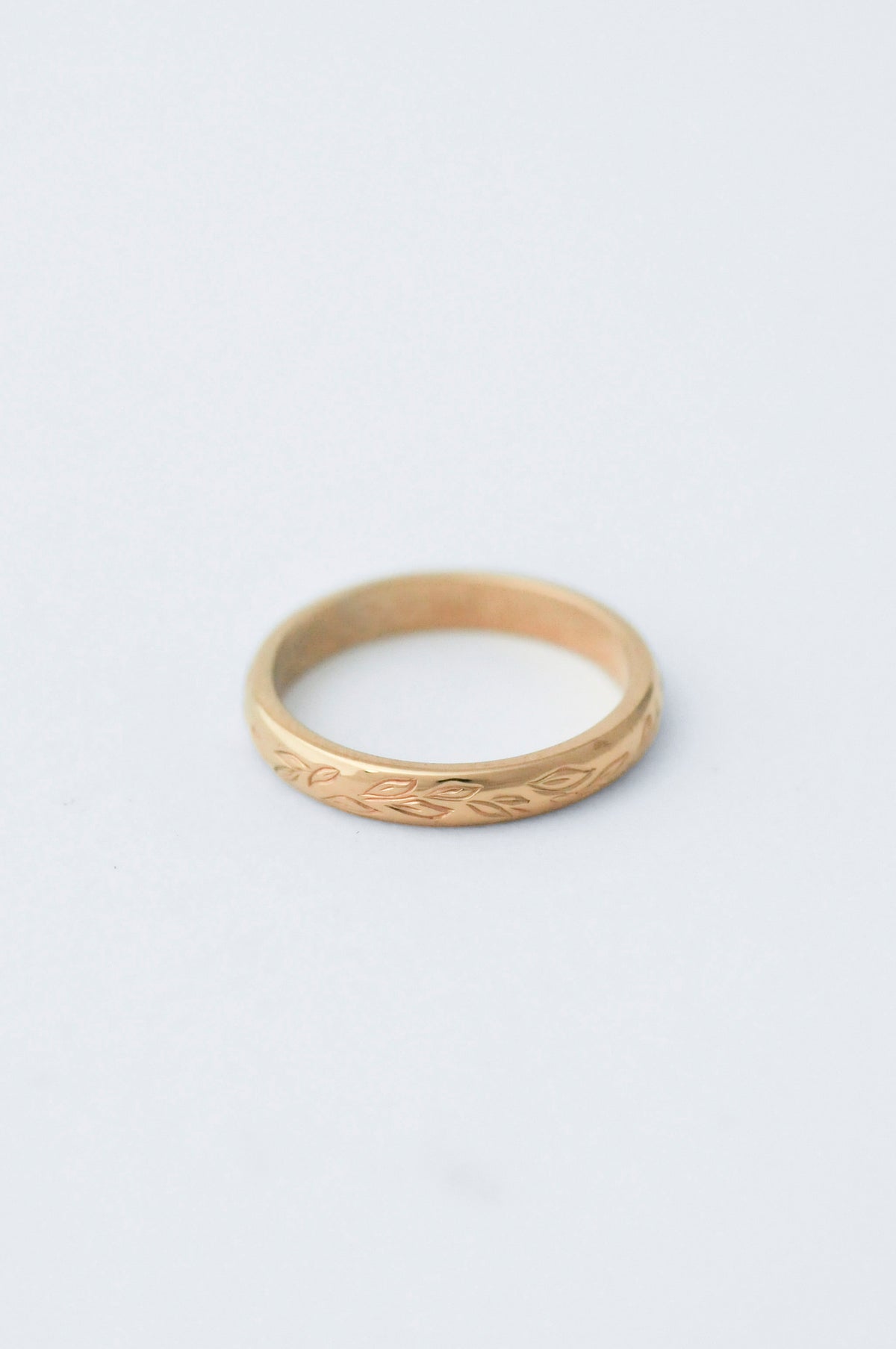 Gold wedding band ring with willow leaf hand engraved detailing on a light grey background