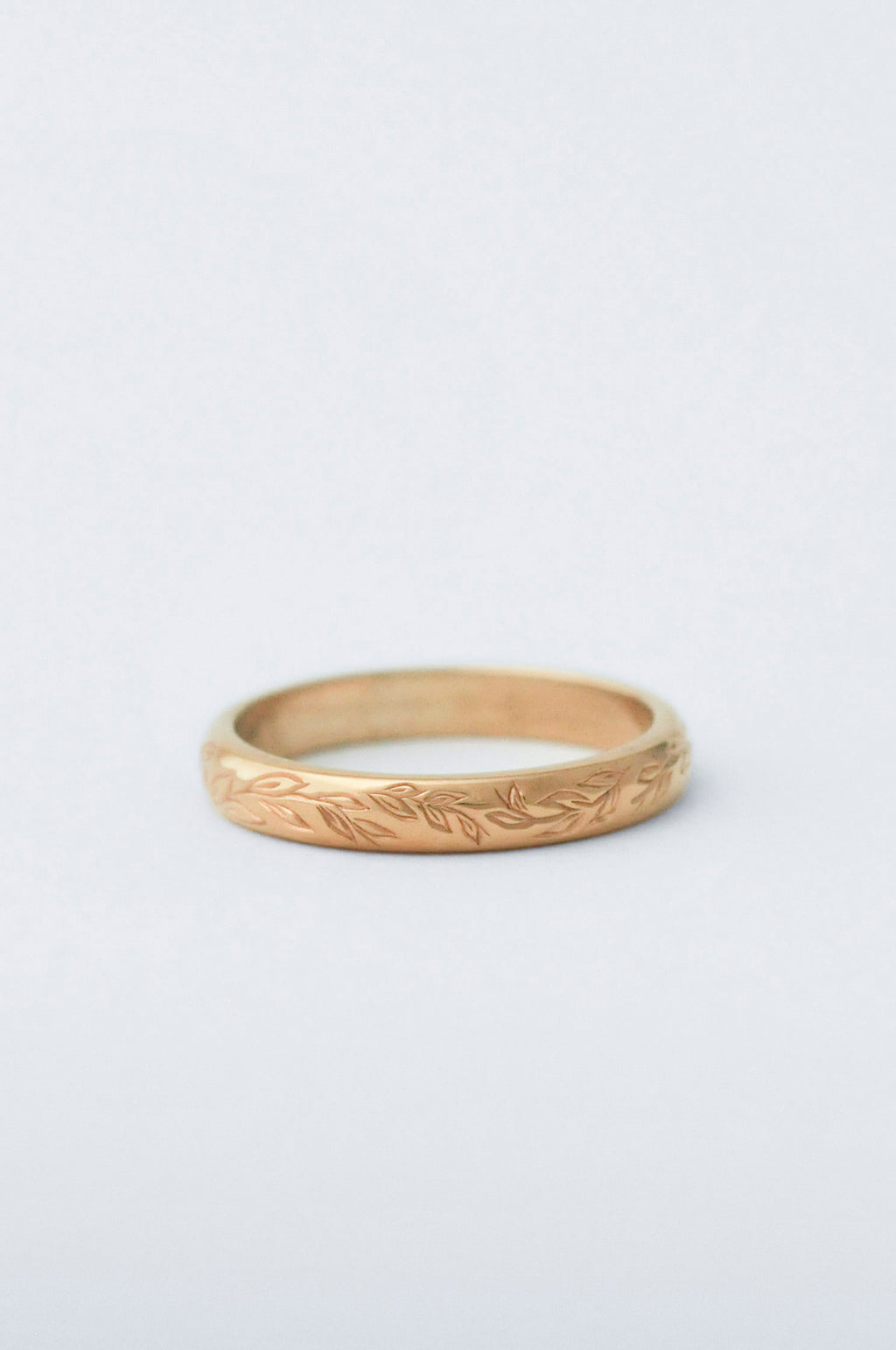 Gold wedding band ring with willow leaf hand engraved detailing on a light grey background
