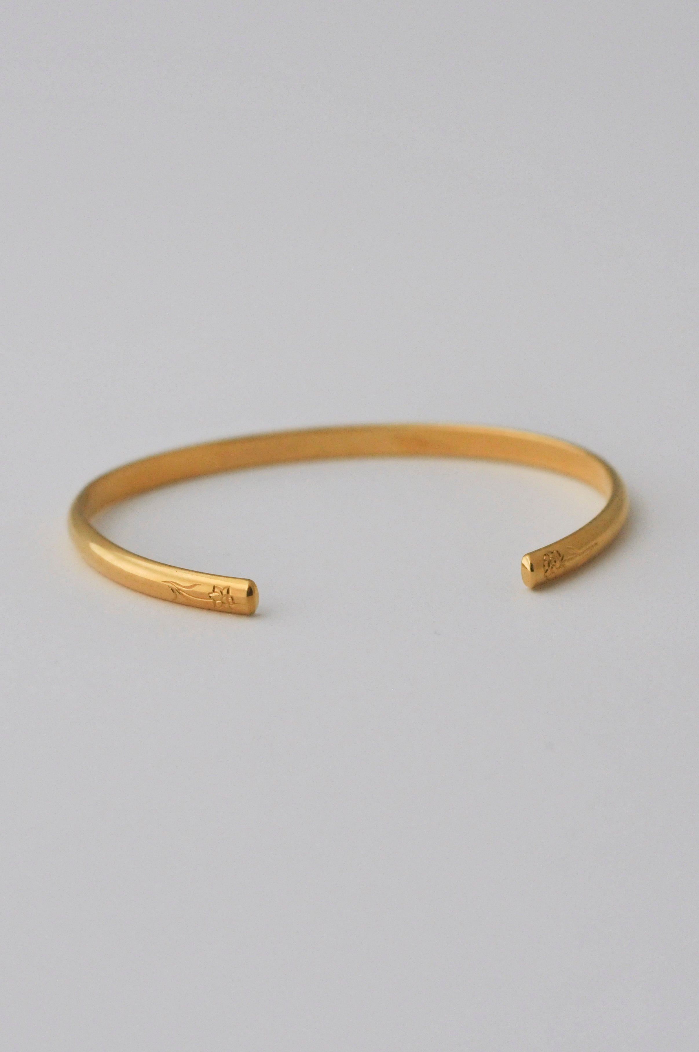 A minimalist vermeil gold open cuff bangle bracelet with hand engraved flowers on each end, photographed on a clean, white background.