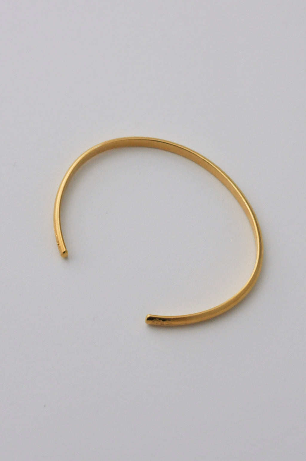 A minimalist vermeil gold open cuff bangle bracelet with hand engraved flowers on each end, photographed on a clean, white background.