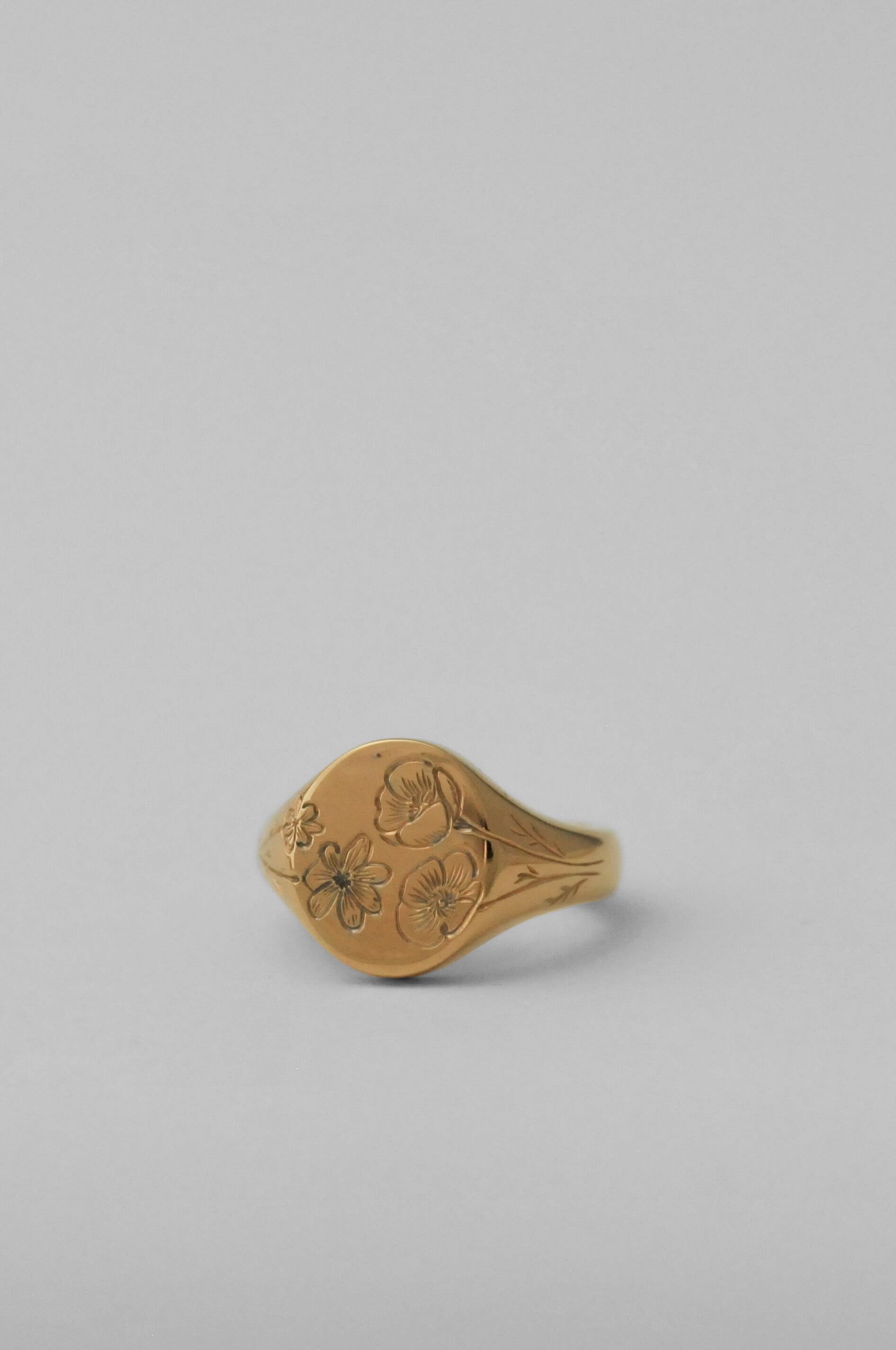 A gold signet ring with two birth flower engravings carved into its oval face set against a solid light grey background.
