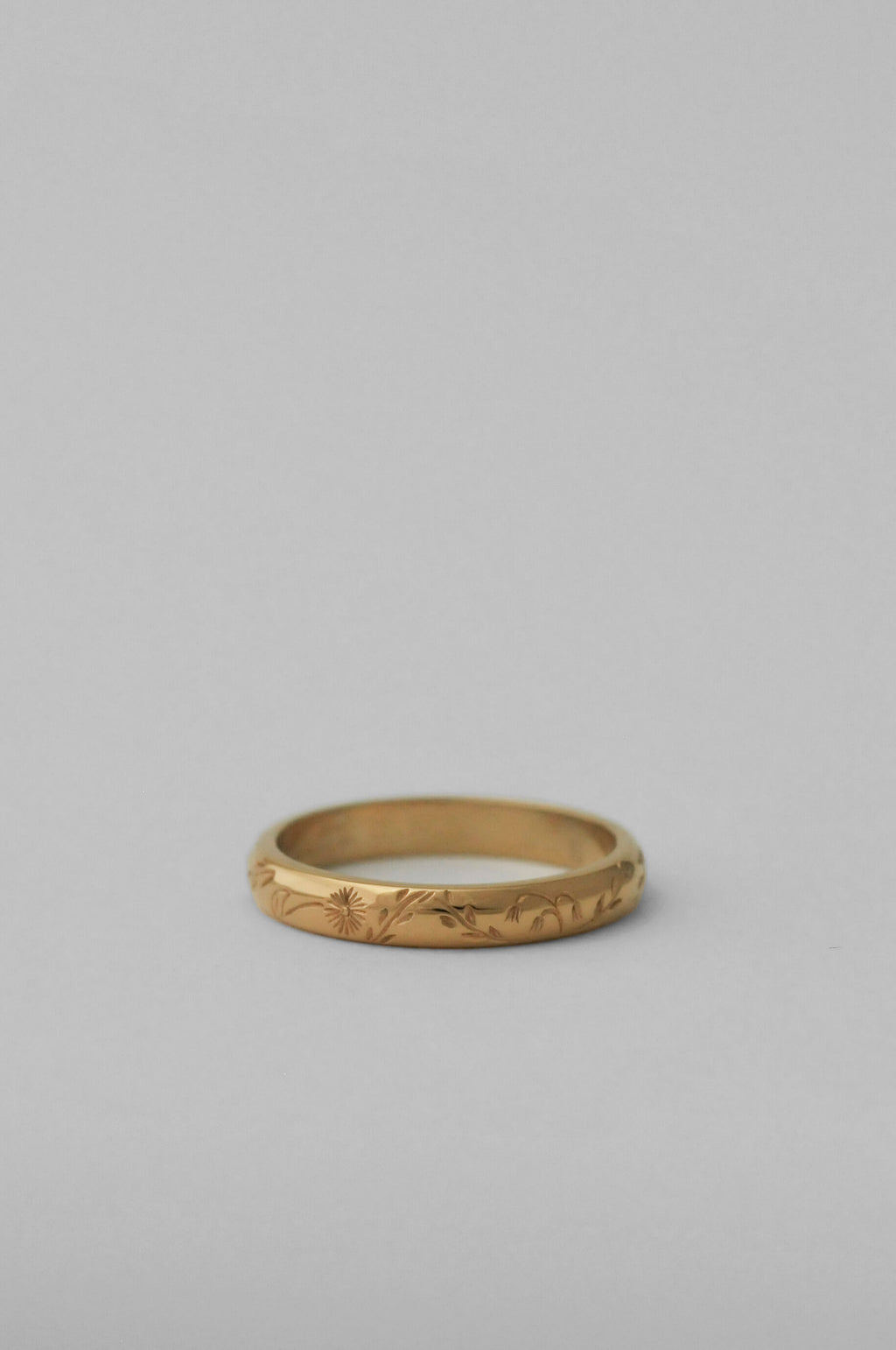 A gold band ring with delicate hand engraved florals, photographed on a neutral white background.