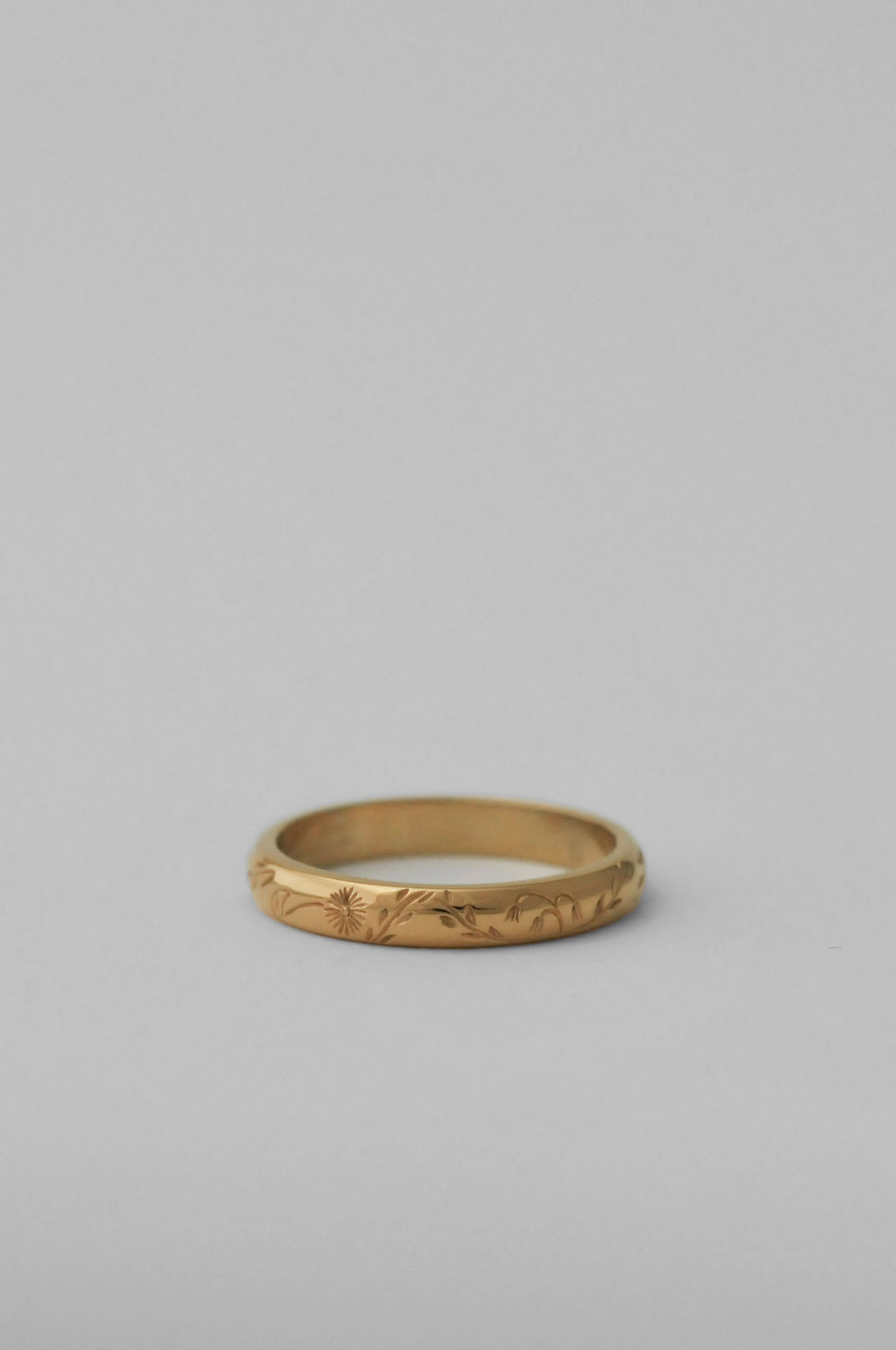 A gold band ring with delicate hand engraved florals, photographed on a neutral white background.