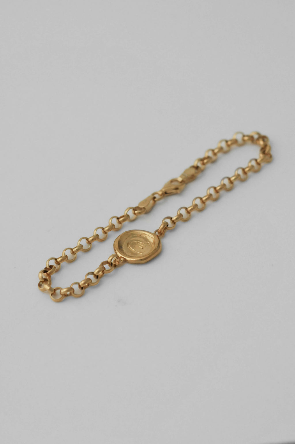 A gold chain bracelet with a round medallion pendant with hand engraved flower, displayed on a natural white background.