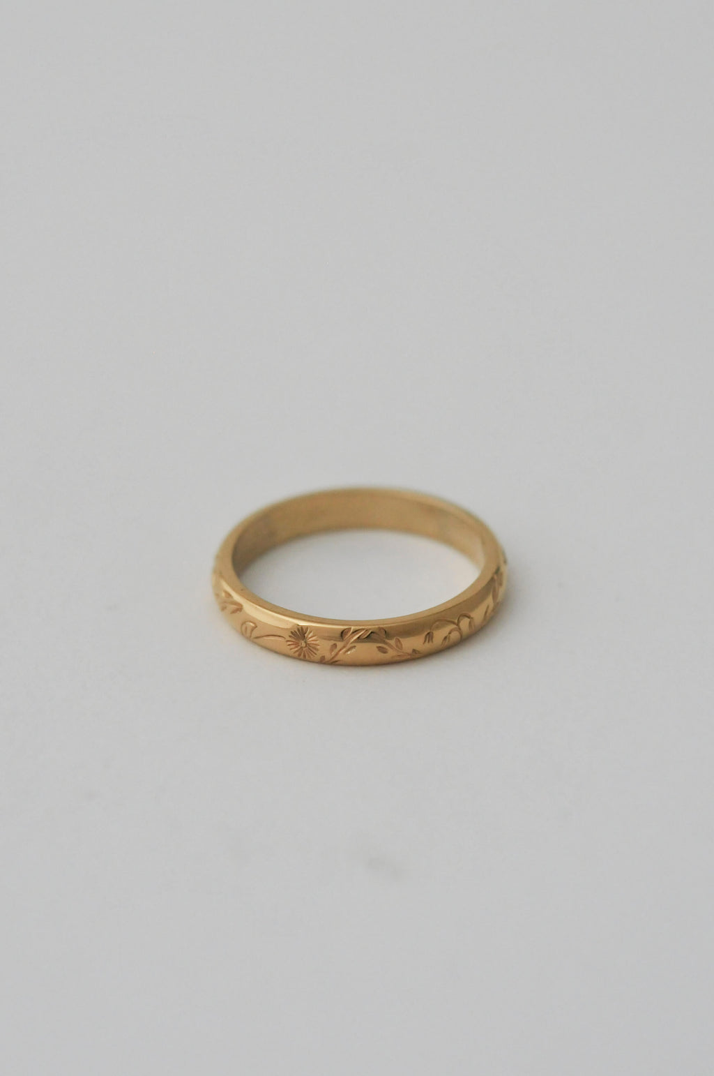 A gold band ring with delicate hand engraved florals, photographed on a neutral white background.