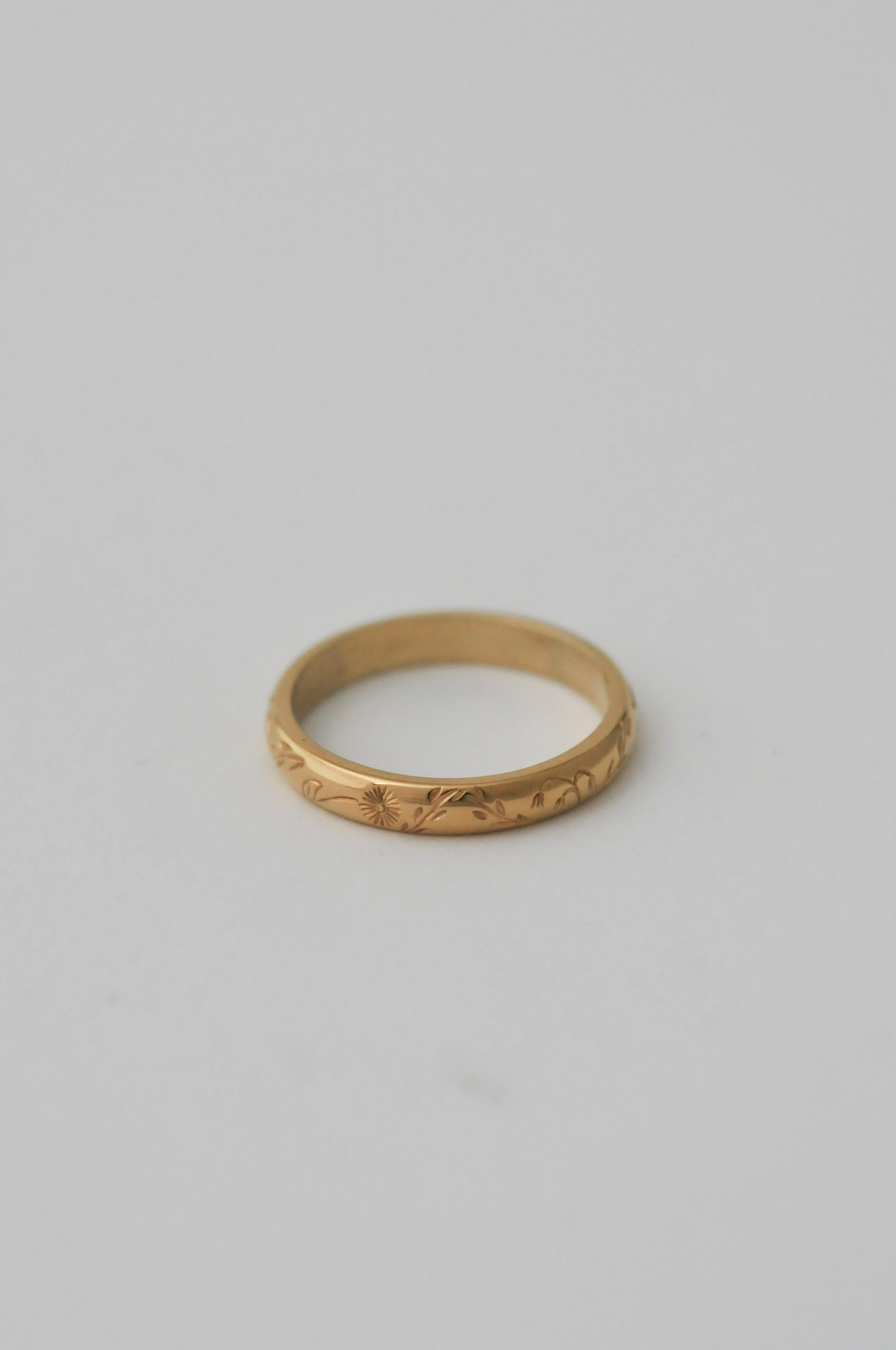 A gold band ring with delicate hand engraved florals, photographed on a neutral white background.