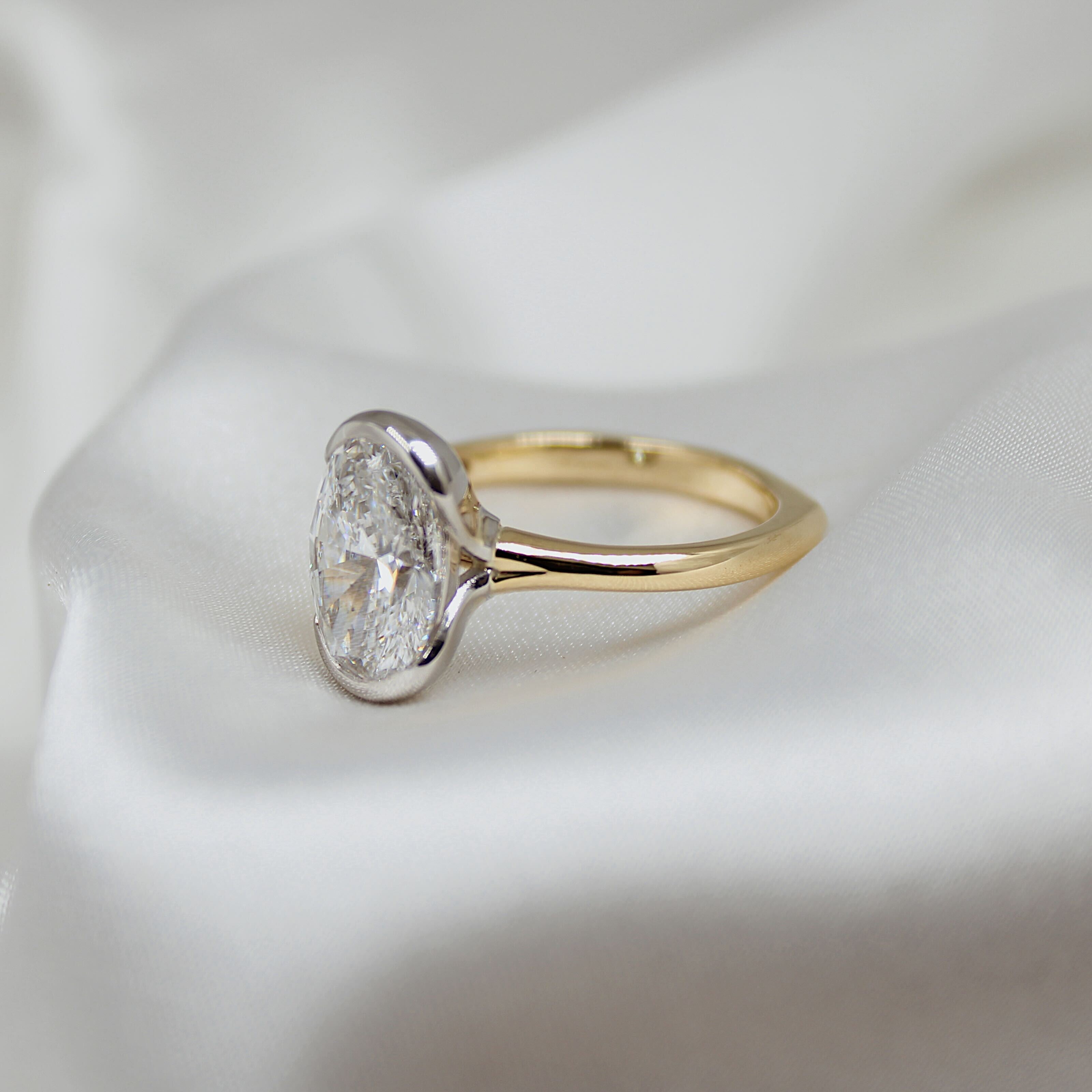 Gold ring with a lab grown oval diamond in a platinum setting on a white background