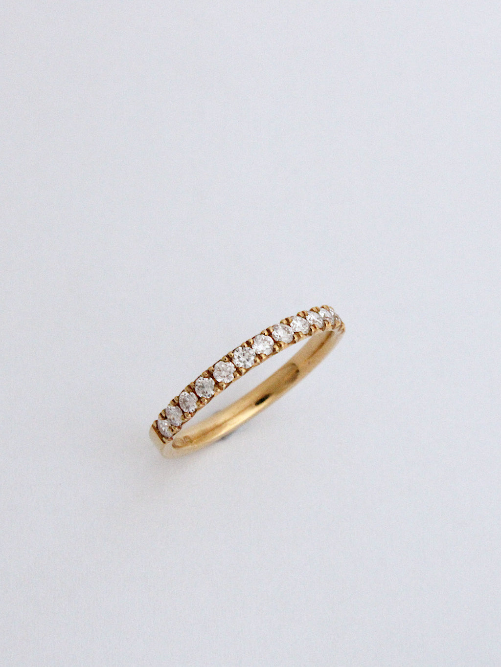 A thin yellow gold eternity ring set with small round-cut diamonds, photographed on a clean, light gray background.