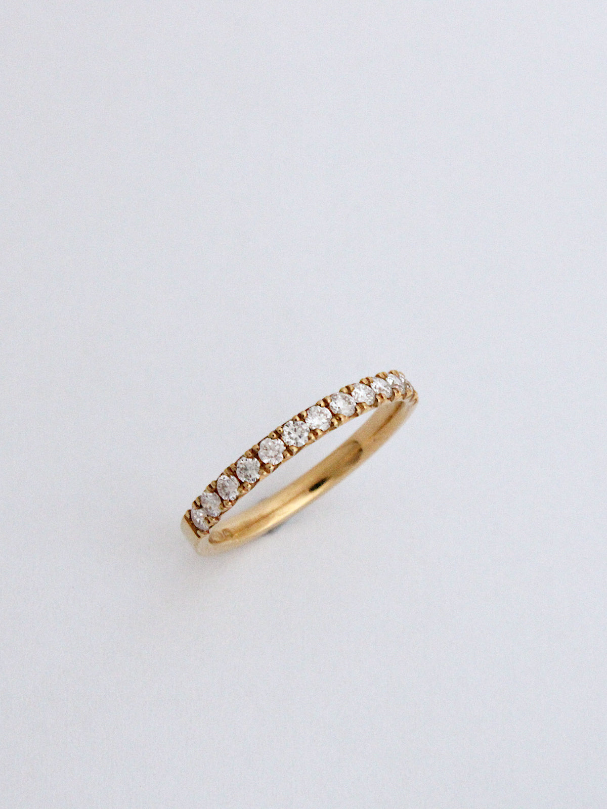 A thin yellow gold eternity ring set with small round-cut diamonds, photographed on a clean, light gray background.