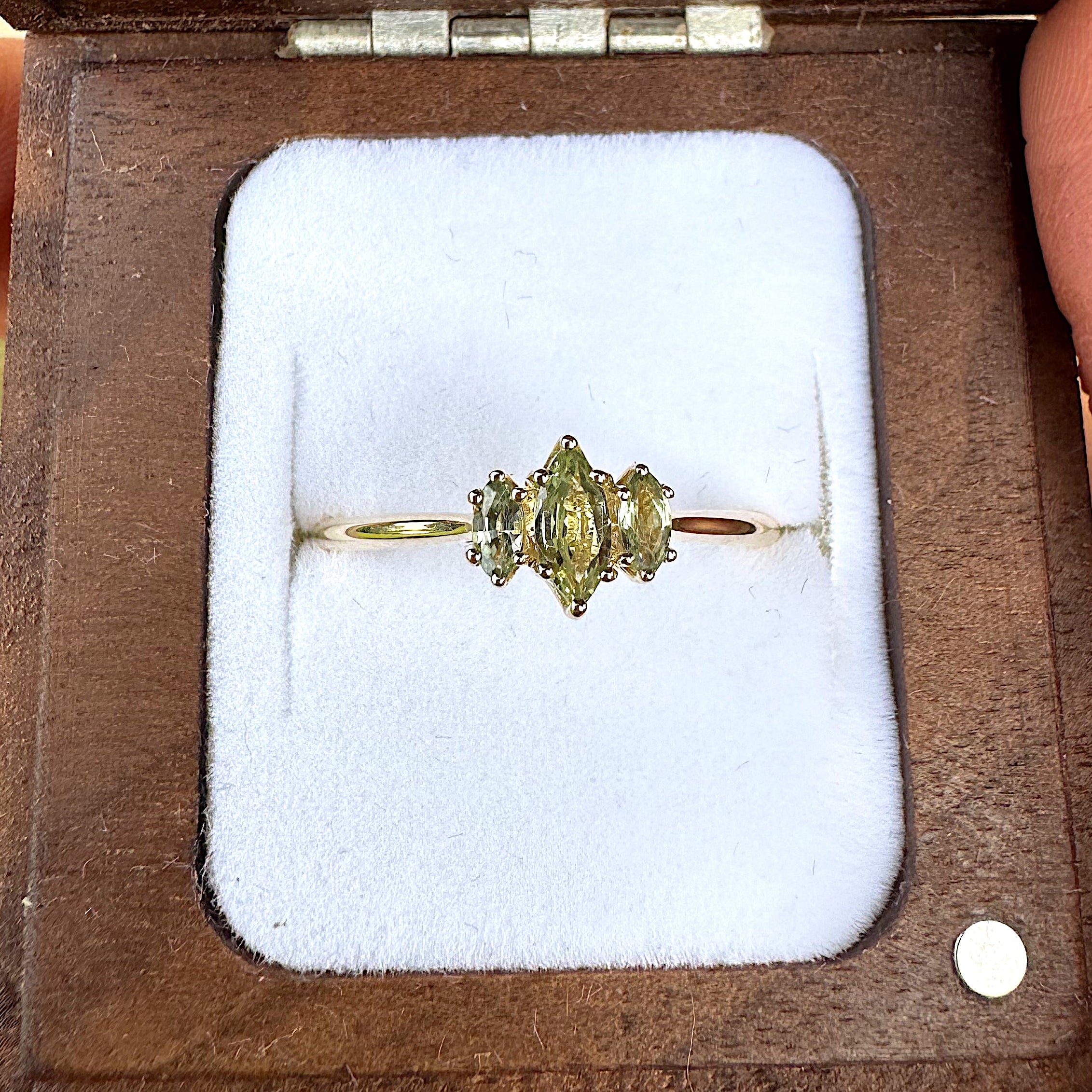 Three stone marquise Gold ring with a green gemstone in a wooden box held by hands.